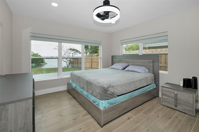 bedroom featuring recessed lighting, a water view, baseboards, and wood finished floors