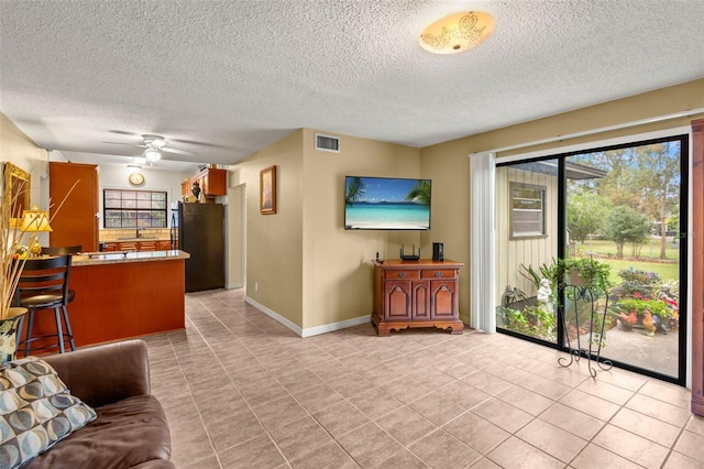 living area featuring a ceiling fan, visible vents, baseboards, and light tile patterned flooring