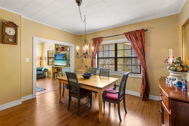 dining room with baseboards, ornamental molding, wood finished floors, and a notable chandelier