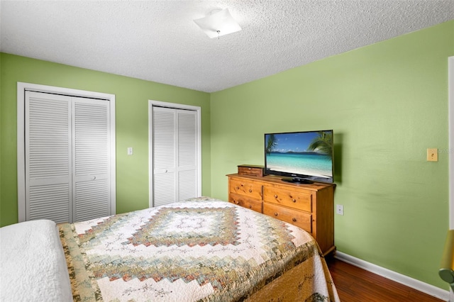 bedroom featuring a textured ceiling, baseboards, two closets, and wood finished floors