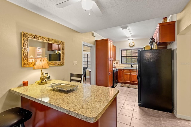 kitchen with a peninsula, a ceiling fan, a sink, freestanding refrigerator, and light countertops