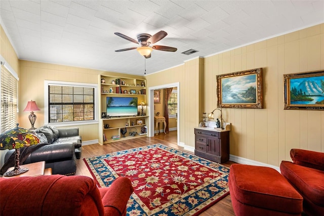living room featuring wood finished floors, visible vents, baseboards, ceiling fan, and ornamental molding