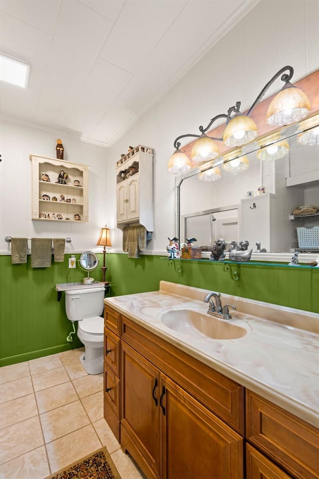 bathroom with toilet, tile patterned floors, vanity, and a wainscoted wall