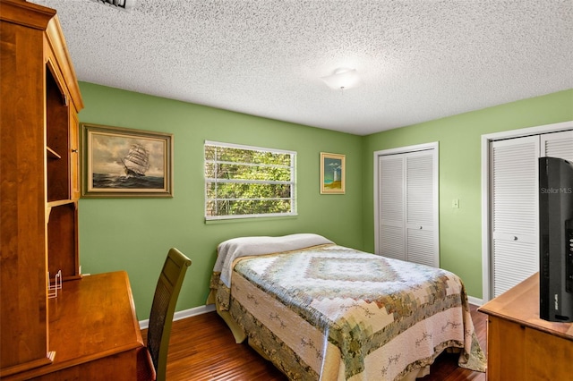 bedroom featuring a textured ceiling, baseboards, multiple closets, and dark wood finished floors