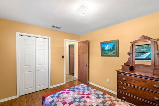 bedroom with a closet, wood finished floors, visible vents, and baseboards