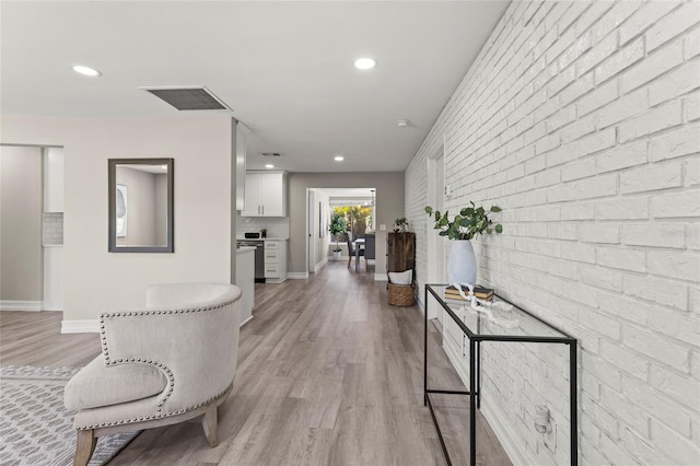 hall with recessed lighting, visible vents, light wood-style flooring, brick wall, and baseboards