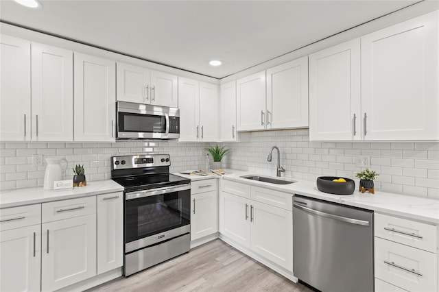 kitchen featuring stainless steel appliances, light wood finished floors, a sink, and white cabinets