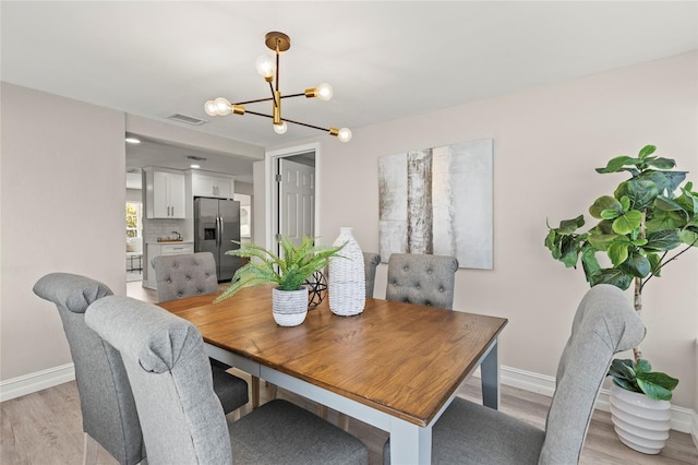 dining space featuring light wood-style flooring, visible vents, a chandelier, and baseboards