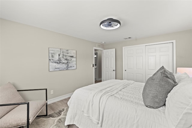 bedroom with a closet, visible vents, baseboards, and wood finished floors