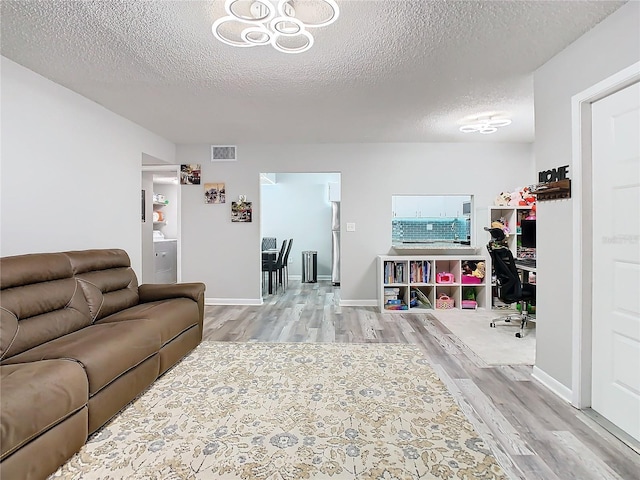 living room with a textured ceiling, baseboards, visible vents, and light wood-style floors