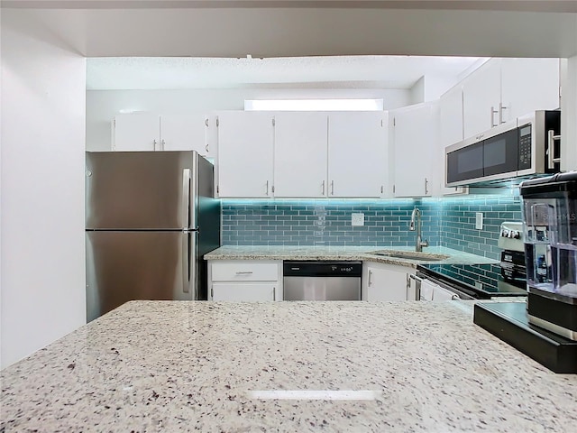 kitchen with appliances with stainless steel finishes, decorative backsplash, a sink, and white cabinets