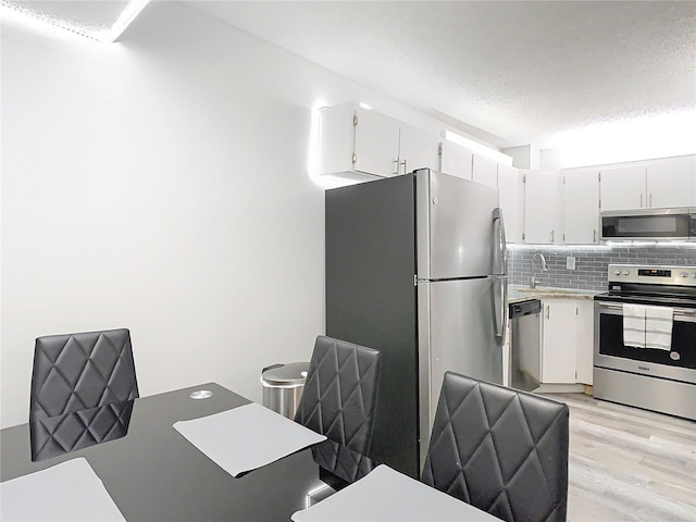 kitchen with stainless steel appliances, light countertops, light wood-style flooring, decorative backsplash, and white cabinets