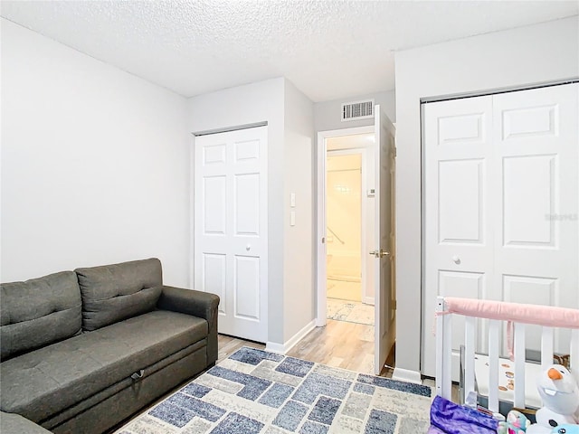 bedroom featuring a textured ceiling, visible vents, baseboards, light wood-style floors, and a nursery area