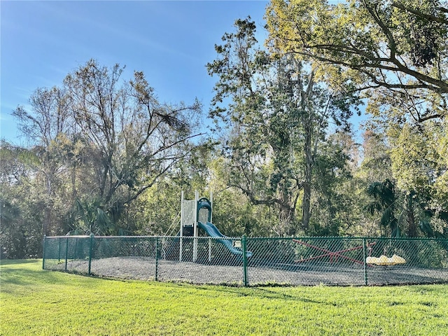 view of tennis court with playground community, fence, and a lawn