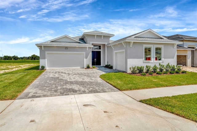 prairie-style house featuring a garage, decorative driveway, a front lawn, and stucco siding