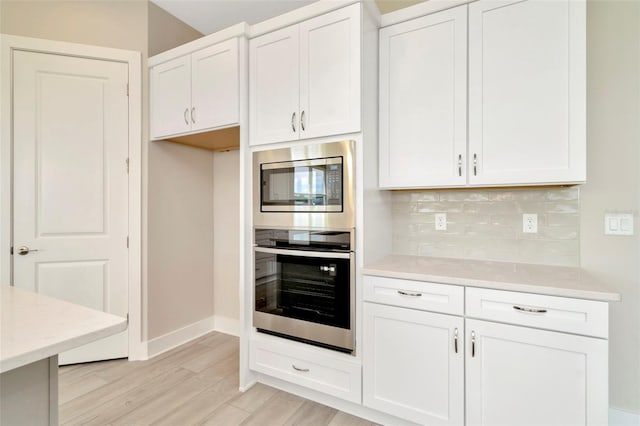 10714 Torchwood Sea Way, San Antonio, FL 33576 - kitchen featuring tasteful backsplash, appliances with stainless steel finishes, light countertops, light wood-type flooring, and white cabinetry