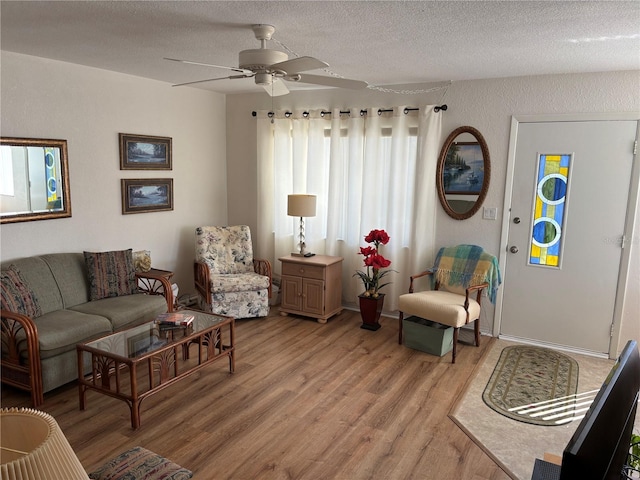 living area featuring a textured ceiling, light wood finished floors, a ceiling fan, and baseboards