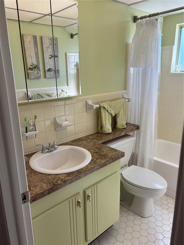 bathroom featuring toilet, shower / tub combo with curtain, tile patterned flooring, vanity, and tile walls