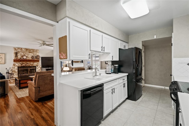 kitchen featuring a stone fireplace, a sink, white cabinets, light countertops, and black appliances