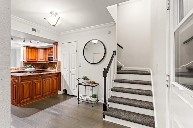 stairway featuring ornamental molding, visible vents, baseboards, and wood finished floors