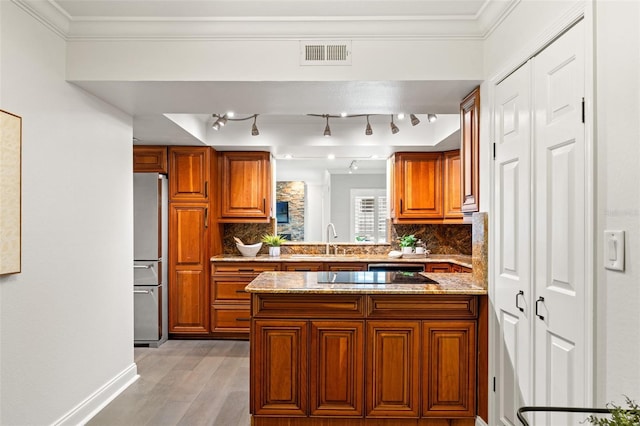 kitchen featuring visible vents, brown cabinetry, freestanding refrigerator, light stone countertops, and a sink