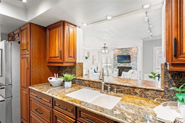 kitchen with brown cabinetry, freestanding refrigerator, light stone countertops, a fireplace, and a sink