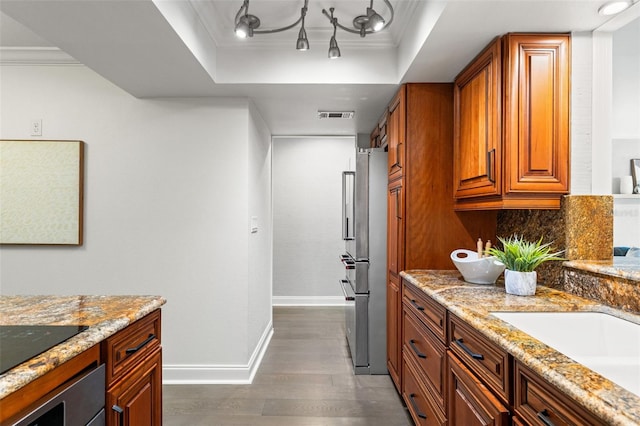 kitchen with dark wood-style floors, a tray ceiling, brown cabinetry, and crown molding