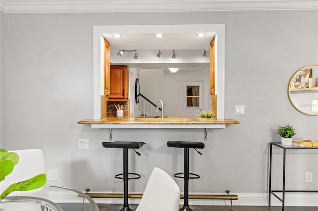 kitchen with baseboards, light stone counters, brown cabinets, a breakfast bar, and crown molding