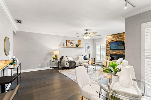 living area with a stone fireplace, visible vents, a ceiling fan, ornamental molding, and dark wood finished floors