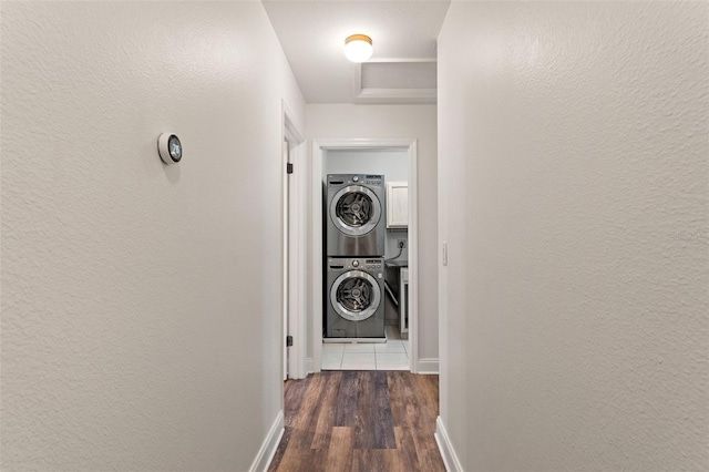 corridor featuring a textured wall, dark wood-style flooring, stacked washing maching and dryer, and baseboards