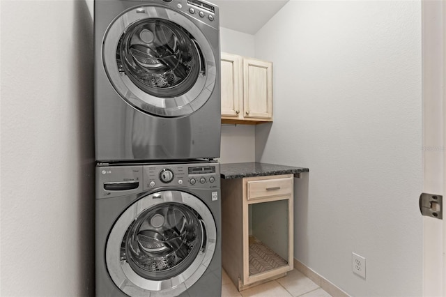 laundry room with stacked washer and dryer, light tile patterned floors, baseboards, and cabinet space