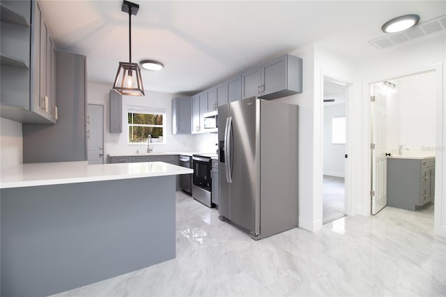 kitchen with a peninsula, a sink, light countertops, appliances with stainless steel finishes, and pendant lighting