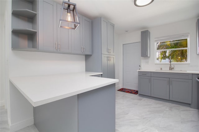 kitchen featuring a sink, hanging light fixtures, light countertops, gray cabinets, and open shelves