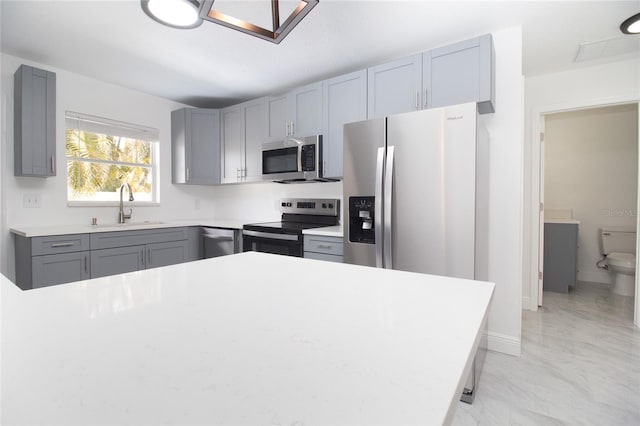 kitchen featuring baseboards, gray cabinets, stainless steel appliances, light countertops, and a sink