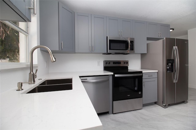 kitchen featuring appliances with stainless steel finishes, gray cabinets, light countertops, and a sink