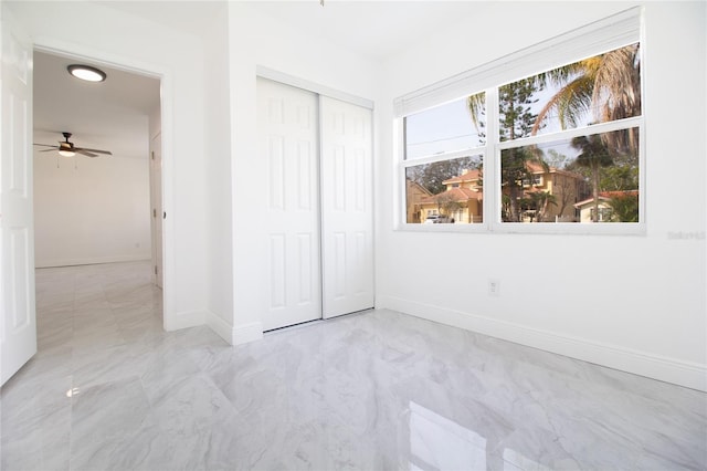 unfurnished bedroom with marble finish floor, a closet, and baseboards