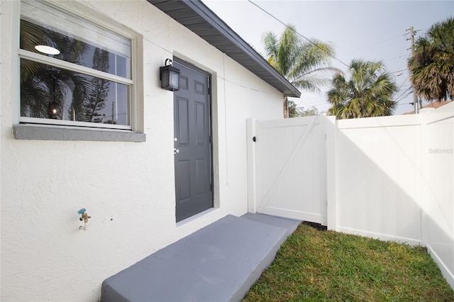 view of exterior entry featuring a gate, fence, and stucco siding