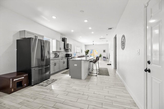 kitchen featuring light stone counters, a breakfast bar, stainless steel appliances, gray cabinetry, and a kitchen island with sink