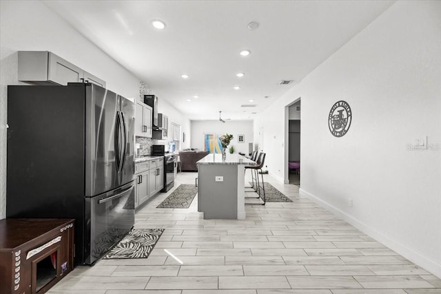 4440 58th Ave N, Saint Petersburg, FL 33714 - kitchen with appliances with stainless steel finishes, a center island, light stone countertops, gray cabinets, and a kitchen bar
