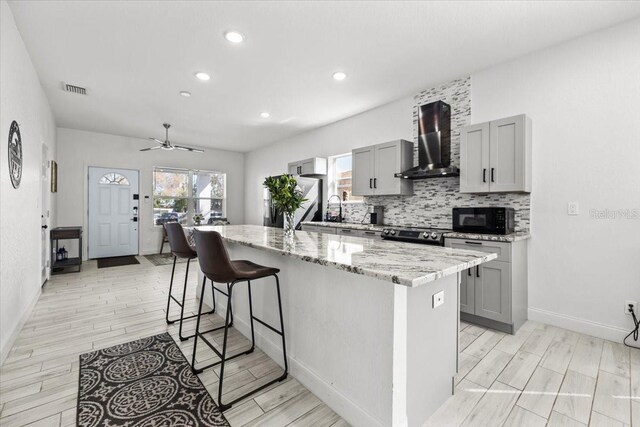 4440 58th Ave N, Saint Petersburg, FL 33714 - kitchen featuring appliances with stainless steel finishes, gray cabinetry, a center island with sink, and wall chimney exhaust hood