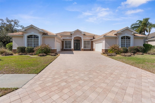 mediterranean / spanish house with a garage, a tiled roof, decorative driveway, and stucco siding