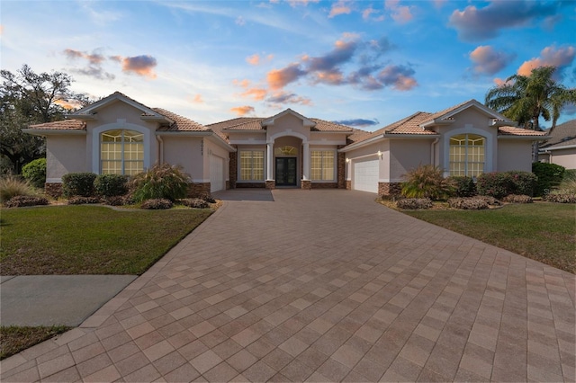 mediterranean / spanish home with stone siding, decorative driveway, an attached garage, and stucco siding