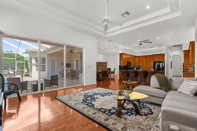 living room featuring a tray ceiling, arched walkways, and crown molding