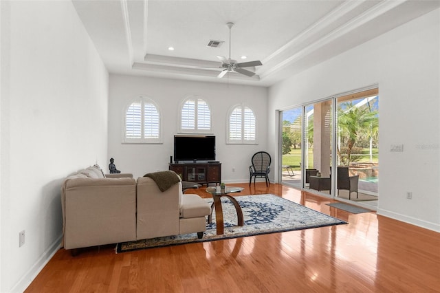 living area with a tray ceiling, wood finished floors, visible vents, and a healthy amount of sunlight