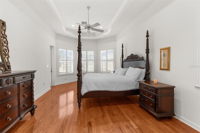 bedroom featuring light wood-style flooring, baseboards, a raised ceiling, and a ceiling fan