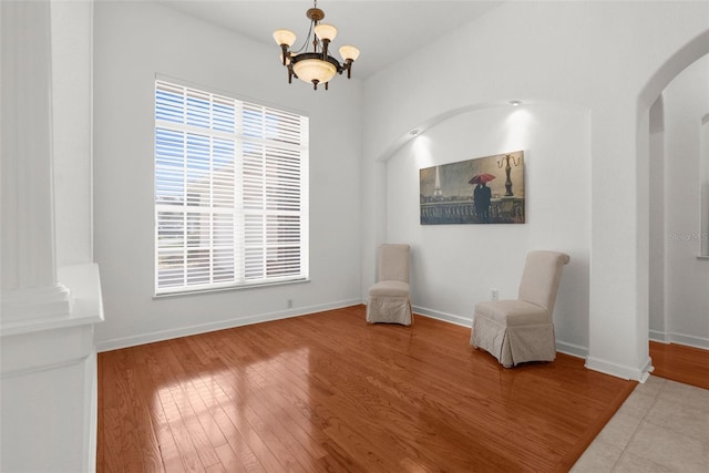 unfurnished room featuring a chandelier, arched walkways, baseboards, and wood finished floors