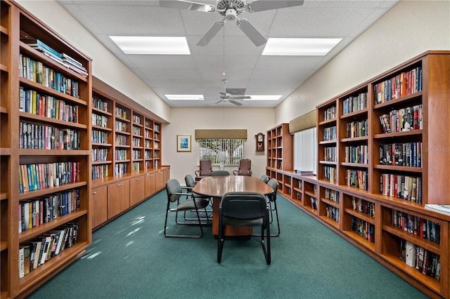 interior space featuring carpet floors, a paneled ceiling, ceiling fan, and wall of books