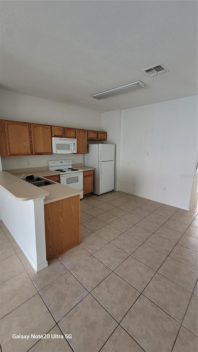 kitchen with white appliances, visible vents, brown cabinetry, a peninsula, and light countertops