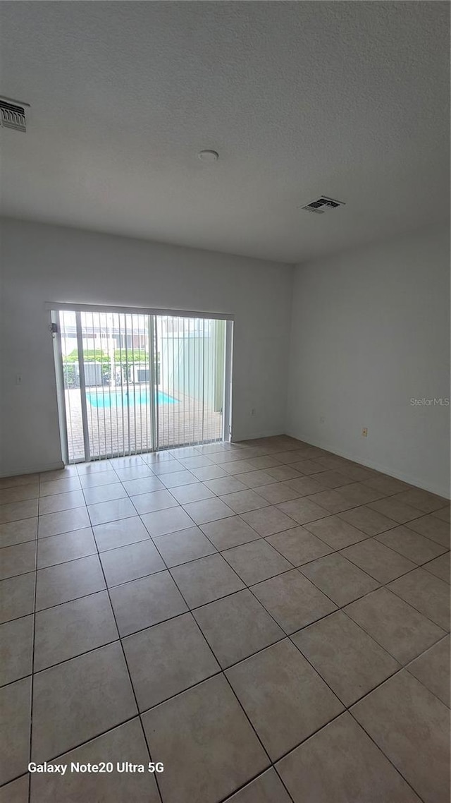 spare room featuring a textured ceiling, light tile patterned floors, and visible vents