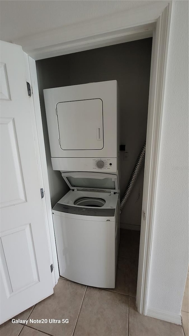 laundry room featuring laundry area, stacked washing maching and dryer, and light tile patterned flooring